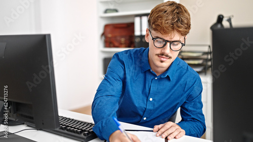 Young hispanic man business worker using computer taking notes at the office