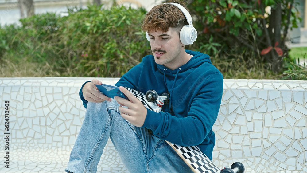 Obraz premium Young hispanic man holding skate playing video game at park