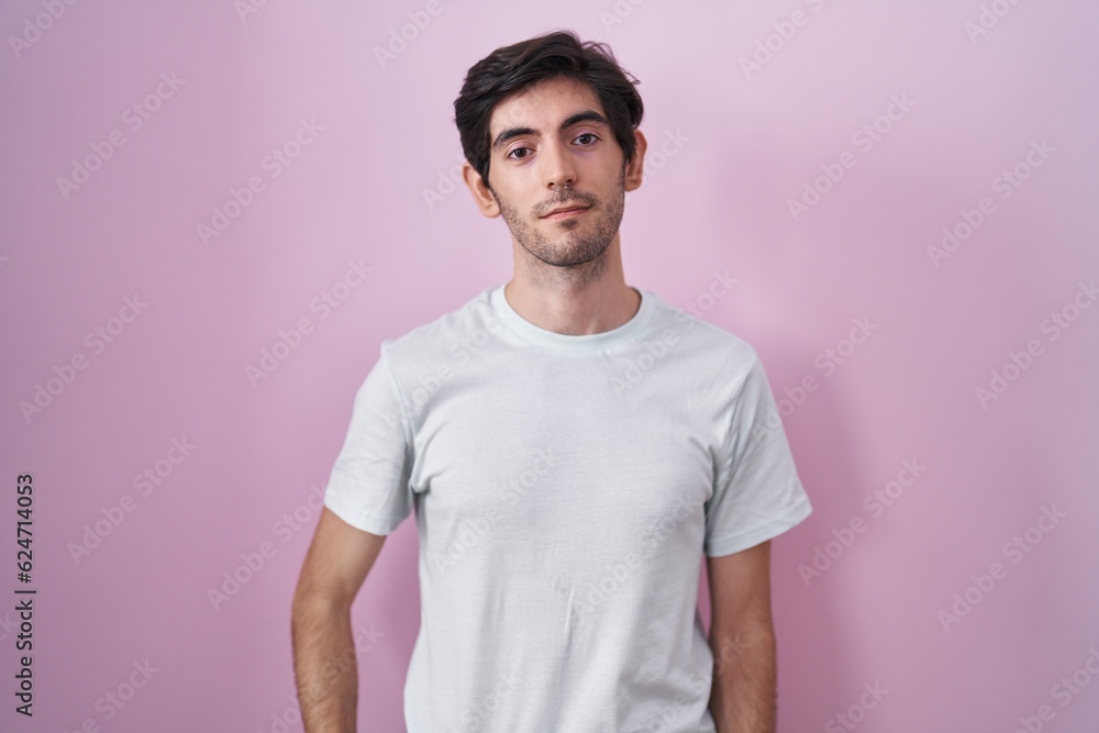 Obraz premium Young hispanic man standing over pink background relaxed with serious expression on face. simple and natural looking at the camera.
