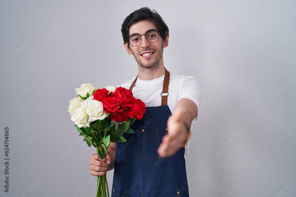 Young hispanic man holding bouquet of white and red roses smiling friendly offering handshake as greeting and welcoming. successful business. Young hispanic man holding bouquet of white and red roses smiling friendly offering handshake as greeting and welcoming. successful business.