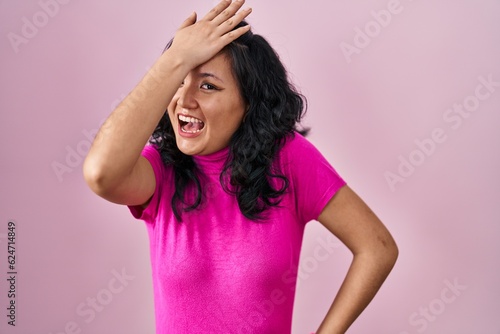 Young asian woman standing over pink background surprised with hand on head for mistake  remember error. forgot  bad memory concept.