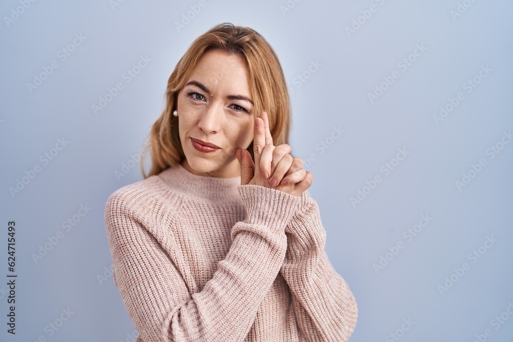 Hispanic woman standing over blue background holding symbolic gun with hand gesture, playing killing shooting weapons, angry face Hispanic woman standing over blue background holding symbolic gun with hand gesture, playing killing shooting weapons, angry face