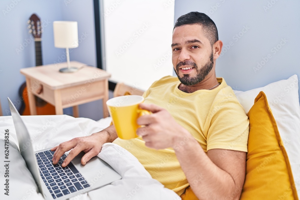 Young latin man using laptop drinking coffee at bedroom Young latin man using laptop drinking coffee at bedroom