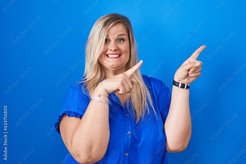 Fototapeta premium Caucasian plus size woman standing over blue background smiling and looking at the camera pointing with two hands and fingers to the side.