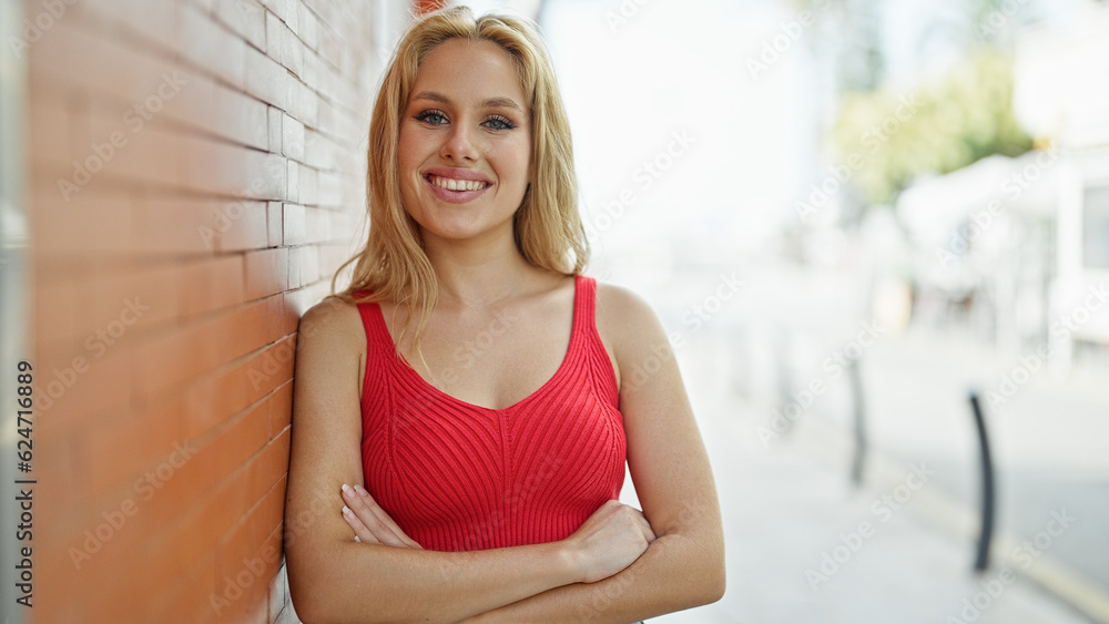 Young blonde woman smiling with crossed arms at street