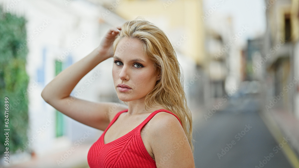 Young blonde woman standing with serious expression combing hair at street