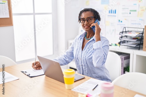 Middle age african american woman business worker talking on smartphone writing on document at office