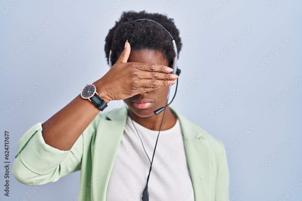 African american woman wearing call center agent headset covering eyes with hand, looking serious and sad. sightless, hiding and rejection concept African american woman wearing call center agent headset covering eyes with hand, looking serious and sad. sightless, hiding and rejection concept