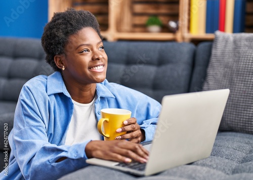 African american woman using laptop and drinking coffee sitting on floor at home