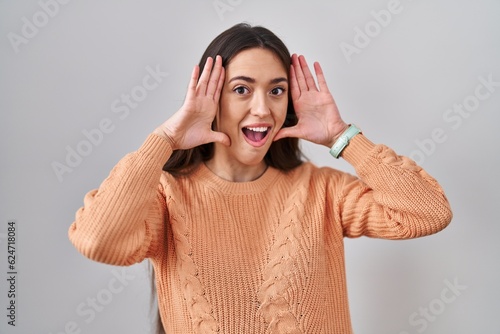Tableau sur toile Young brunette woman standing over white background smiling cheerful playing peek a boo with hands showing face