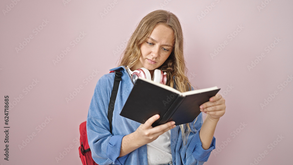Young blonde woman student reading book with serious expression over isolated pink background Young blonde woman student reading book with serious expression over isolated pink background