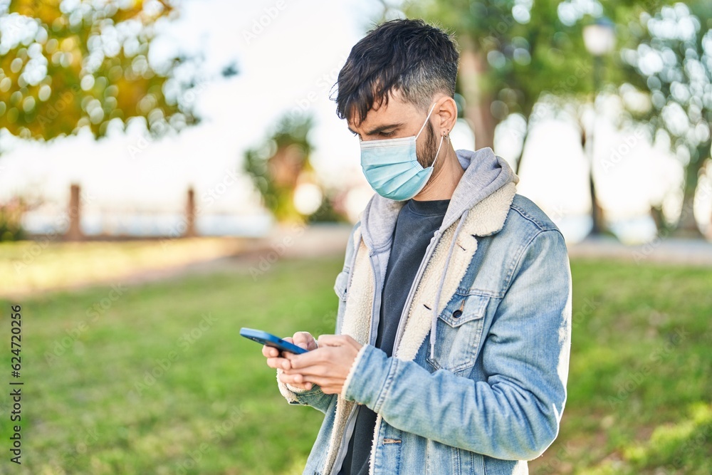 Young hispanic man wearing medical mask using smartphone at park Young hispanic man wearing medical mask using smartphone at park