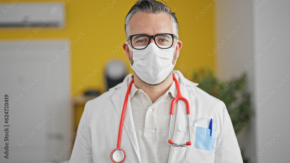 Grey-haired man doctor wearing medical mask standing at the clinic Grey-haired man doctor wearing medical mask standing at the clinic