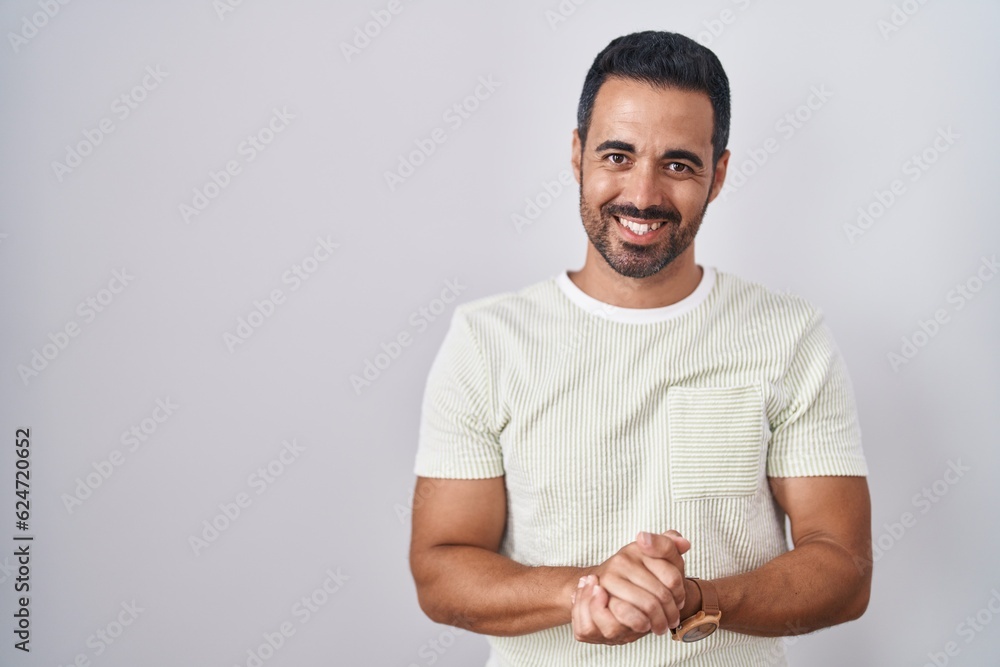 Hispanic man with beard standing over isolated background with hands together and crossed fingers smiling relaxed and cheerful. success and optimistic Hispanic man with beard standing over isolated background with hands together and crossed fingers smiling relaxed and cheerful. success and optimistic