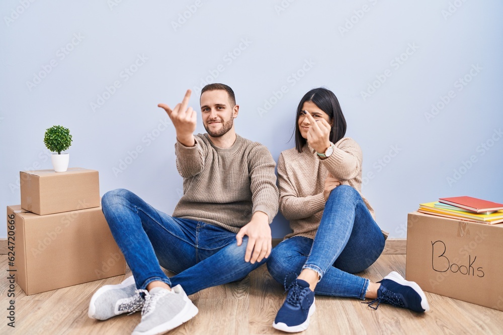Young couple moving to a new home showing middle finger, impolite and rude fuck off expression Young couple moving to a new home showing middle finger, impolite and rude fuck off expression
