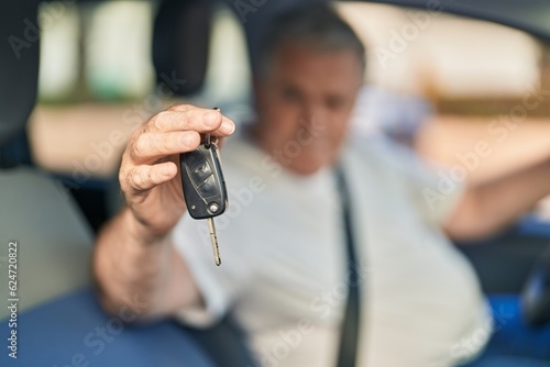 Middle age grey-haired man holding key sitting on car at street
