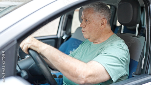 Middle age grey-haired man driving car at street
