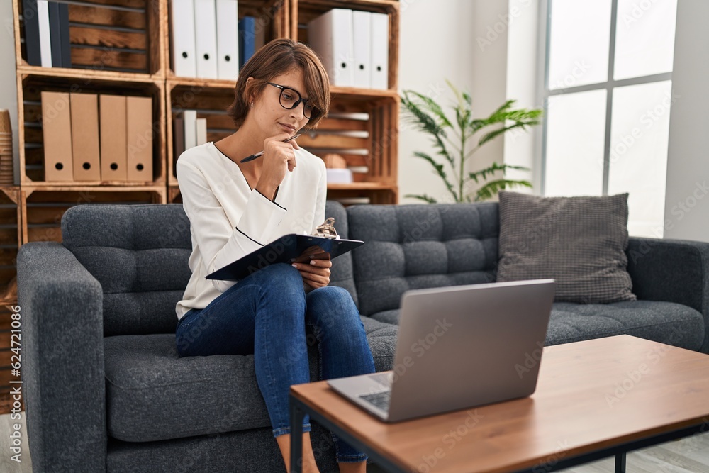 Young beautiful hispanic woman psychologist writing on document using laptop at psychology clinic Young beautiful hispanic woman psychologist writing on document using laptop at psychology clinic
