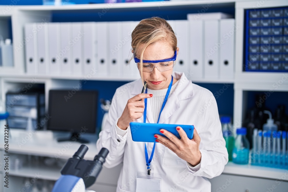 Young blonde woman scientist using touchpad with doubt expression at laboratory Young blonde woman scientist using touchpad with doubt expression at laboratory