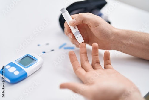 Young caucasian man measuring glucose sitting on table at home