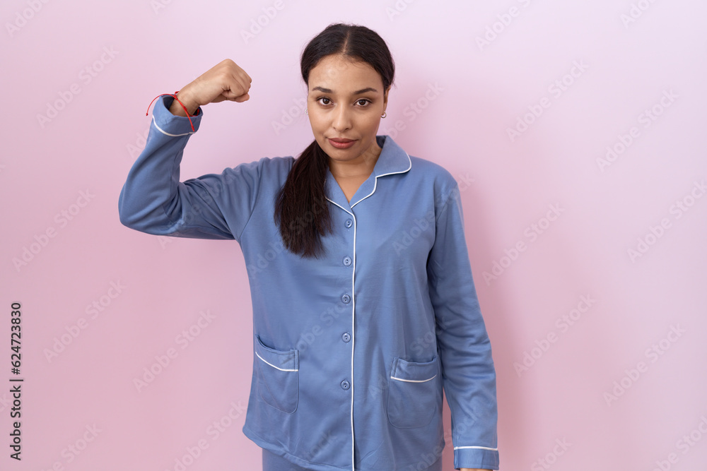 Young arab woman wearing blue pajama strong person showing arm muscle, confident and proud of power Young arab woman wearing blue pajama strong person showing arm muscle, confident and proud of power