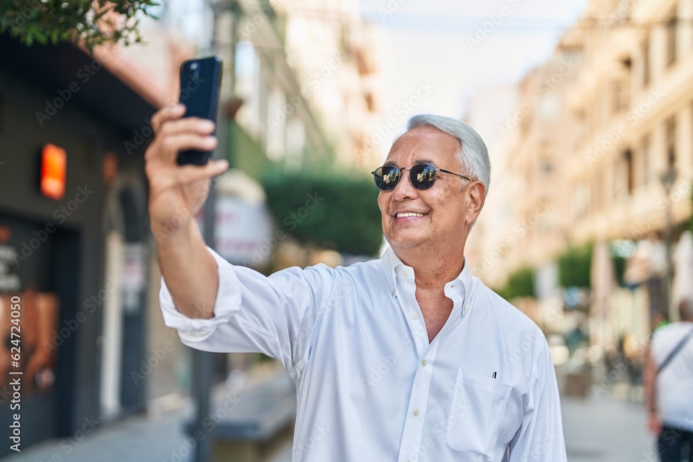 Middle age grey-haired man smiling confident making selfie by the smartphone at street Middle age grey-haired man smiling confident making selfie by the smartphone at street