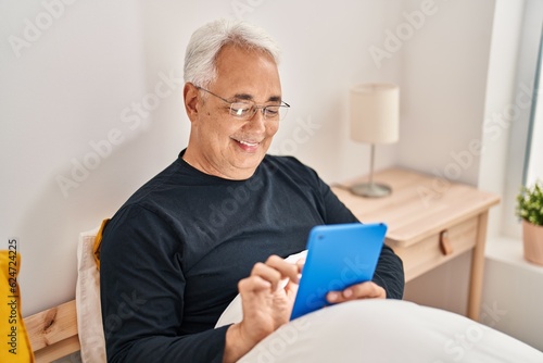 Senior man using touchpad sitting on bed at bedroom © Krakenimages.com