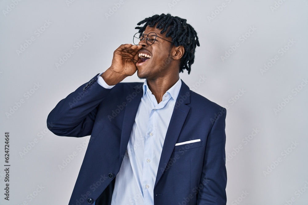 Young african man with dreadlocks wearing business jacket over white background shouting and screaming loud to side with hand on mouth. communication concept. Young african man with dreadlocks wearing business jacket over white background shouting and screaming loud to side with hand on mouth. communication concept.