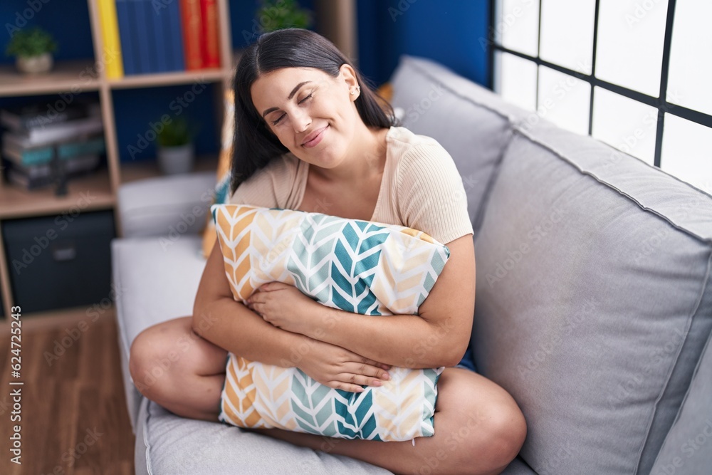 Young beautiful hispanic woman hugging cushion sitting on sofa at home Young beautiful hispanic woman hugging cushion sitting on sofa at home