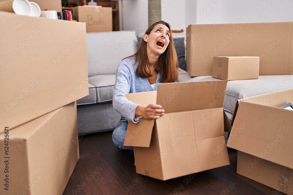 Young woman moving to a new home looking inside cardboard box angry and mad screaming frustrated and furious, shouting with anger looking up. Young woman moving to a new home looking inside cardboard box angry and mad screaming frustrated and furious, shouting with anger looking up.