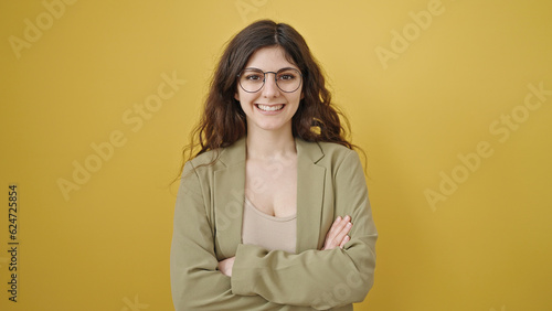 Young beautiful hispanic woman smiling confident standing with arms crossed gesture over isolated yellow background