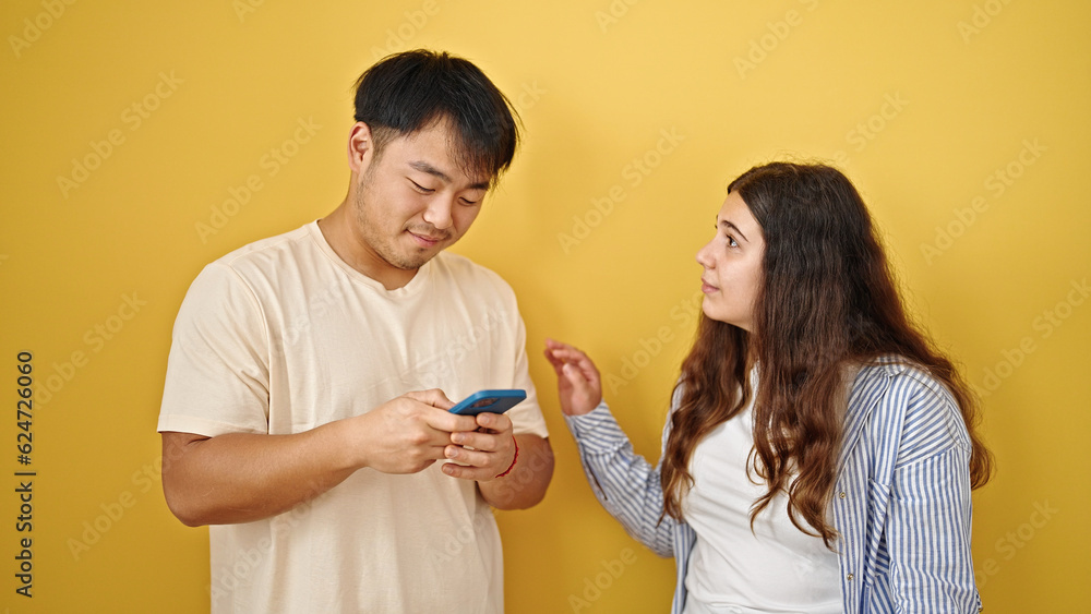 Man and woman couple using smartphones with serious expression over isolated yellow background Man and woman couple using smartphones with serious expression over isolated yellow background