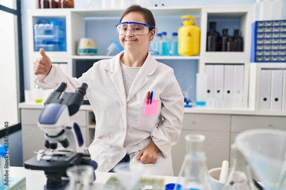Hispanic girl with down syndrome working at scientist laboratory looking proud, smiling doing thumbs up gesture to the side Hispanic girl with down syndrome working at scientist laboratory looking proud, smiling doing thumbs up gesture to the side