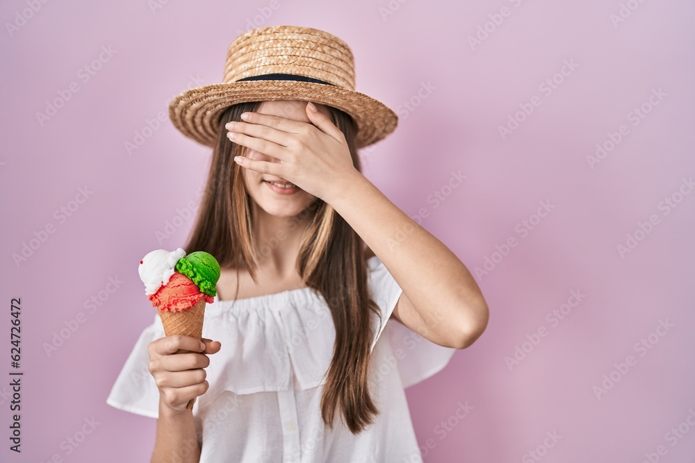 Teenager girl holding ice cream smiling and laughing with hand on face covering eyes for surprise. blind concept.