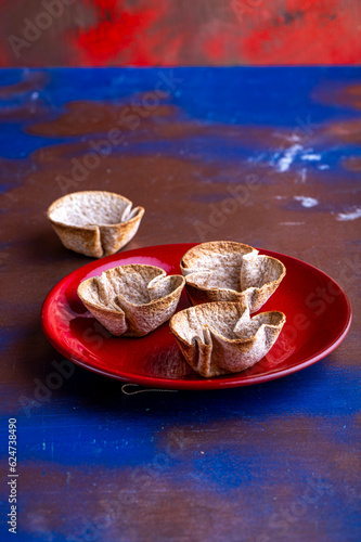 Dried tortilla cups on a red plate against a textured background.