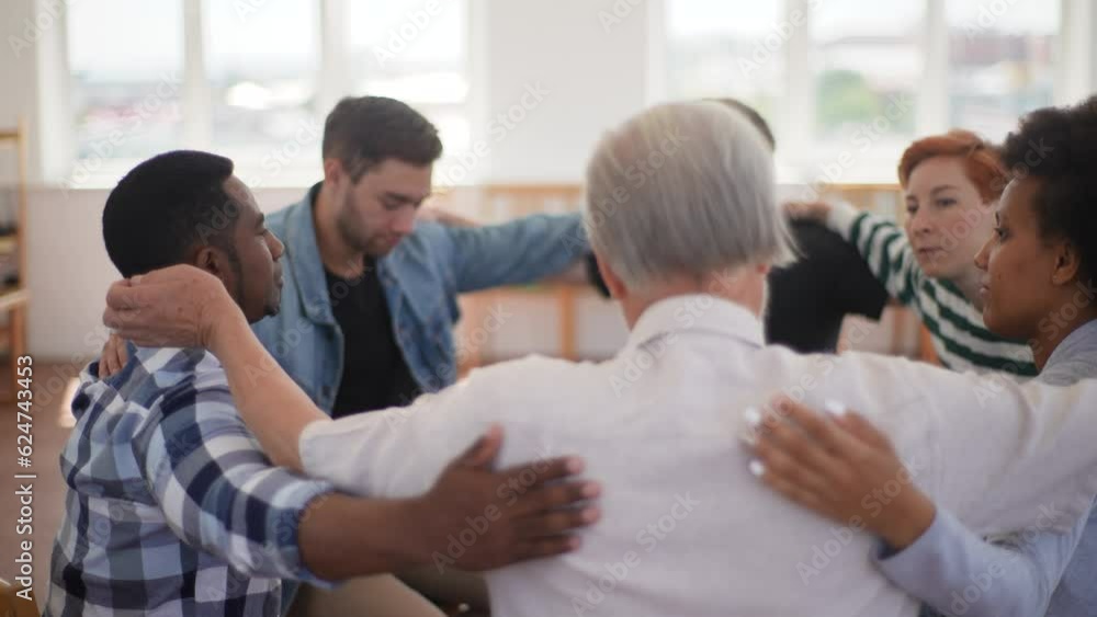 Concept of support and help. Multicultural and different ages group of addicted people discuss problems and together holding shoulders each other on therapy sitting on chairs in circle, slow motion. Concept of support and help. Multicultural and different ages group of addicted people discuss problems and together holding shoulders each other on therapy sitting on chairs in circle, slow motion.