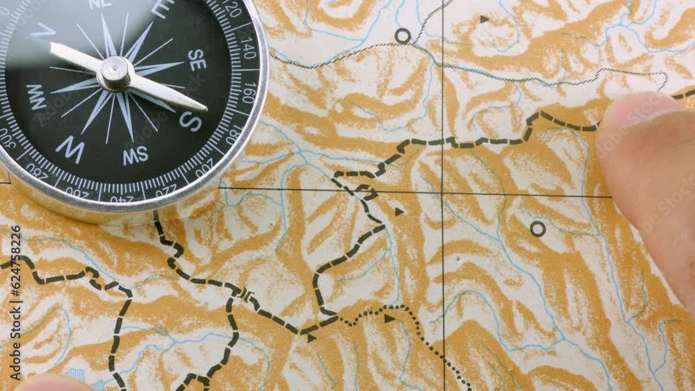 Close up male finger following route on blank map with compass Close up male finger following route on blank map with compass