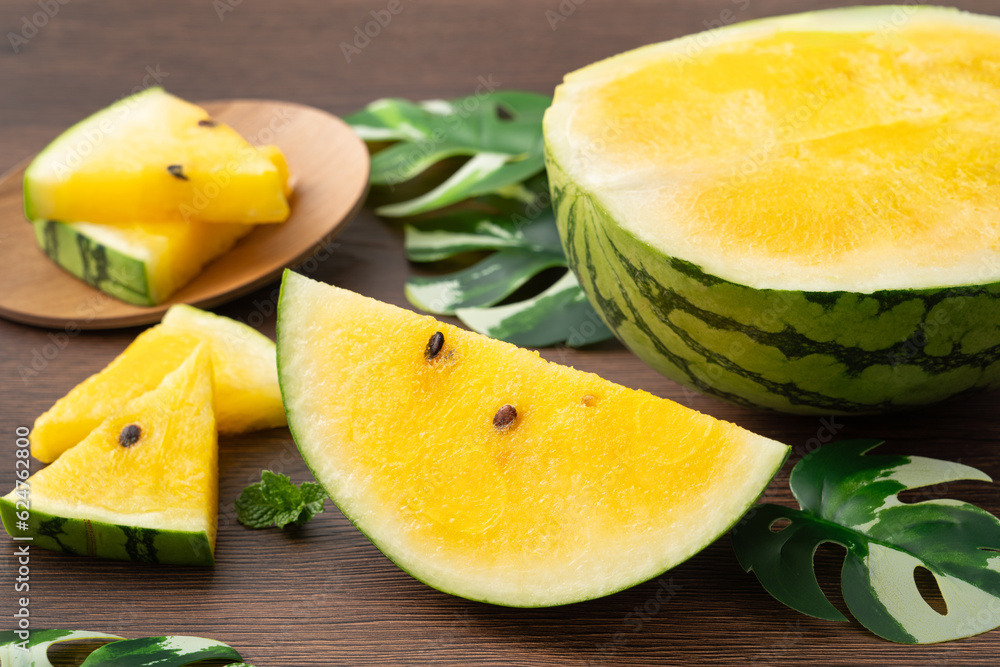 Sliced yellow watermelon in a plate on wooden table background.