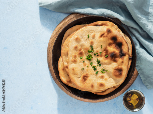 Stack of fesh naan breads in cast-iron pan on blue background with copy space. Top view of perfect naan flatbreads in black circle cast iron pan photo