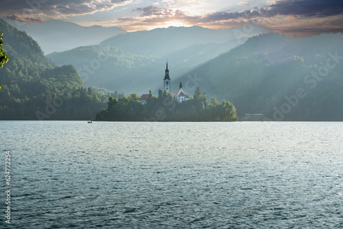 Lake Bled in Slovenia. Beautiful mountain lake with small Pilgrimage Church. Spectacular mountains and cloudy sky in the background in backlight. Backlight shooting in photography © Bulent