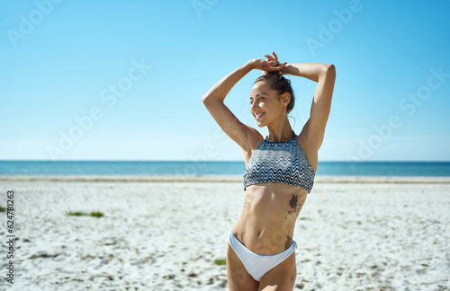 Charming bikini woman with tanned perfect body posing on sunny beach with white sand. This concept of tanned skin  hair removal  beauty of smooth skin and body care