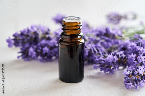 Essential oil bottle with lavender blossoms on bright background
