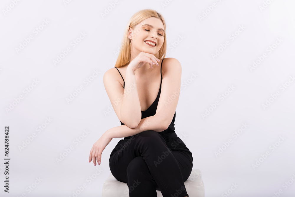 Portrait of a young, elegant, happy and smiling girl sitting on a pouf on a white background. Portrait of a young, elegant, happy and smiling girl sitting on a pouf on a white background.