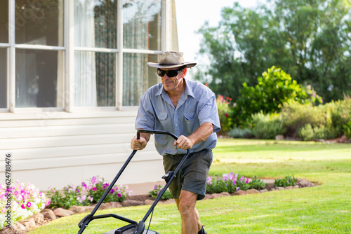 Middle aged australian man pushing lawn mower mowing grass of house front yard photo