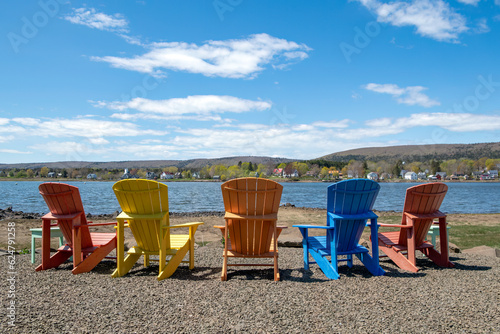 Colorful painted wood deck chairs on a gravel shore of a harbor on the east coast of Canada.