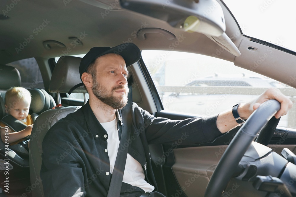 A man driving a car and a small child toddler in the back seat in a car seat