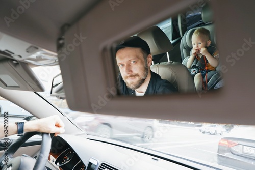 A man driving a car looks in the mirror at a toddler child in the back seat in a child car seat