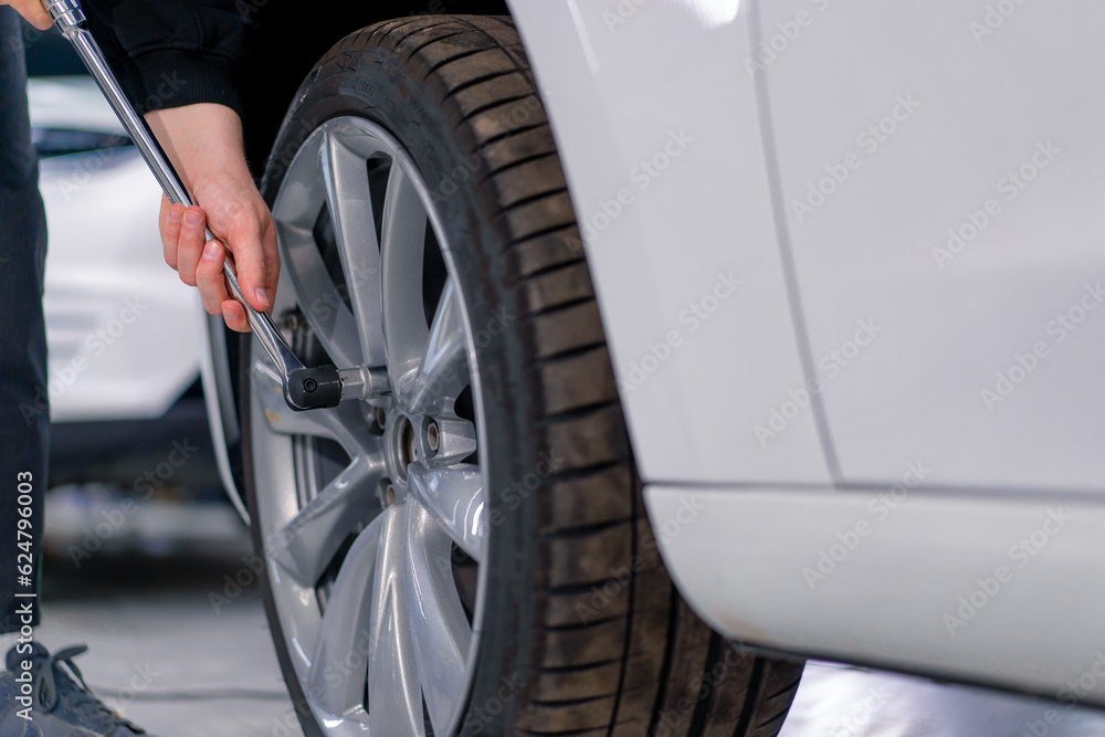 Auto mechanic man changing a wheel on a luxury white car using a balloon wrench at a car service station close-up