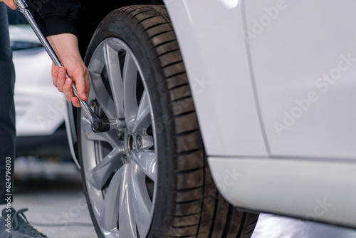 Auto mechanic man changing a wheel on a luxury white car using a balloon wrench at a car service station close-up © Guys Who Shoot