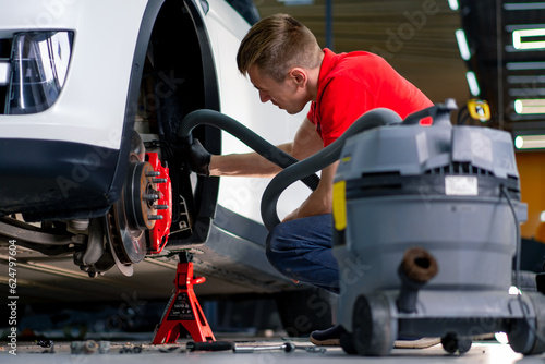 Tableau sur toile A man in gloves car service worker cleaning fender liner with vacuum cleaner dur